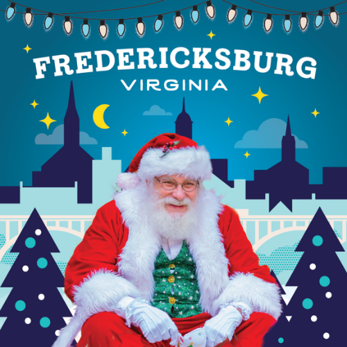 Santa sitting in front of Fredericksburg blue backdrop with the city skyline and festive trees