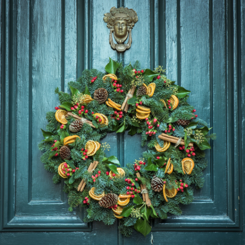 holiday day wreath decorated with pine cones, holly berries and orange slices on a green door