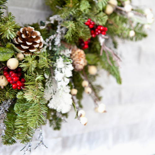 close up image of a green evergreen wreath with snow on the wreath. Wreath is decorated with pine cones and holiday berries.