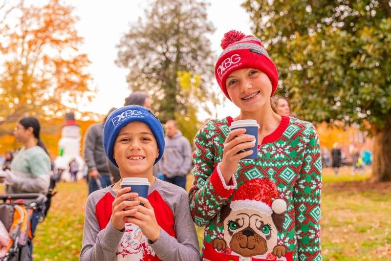 boy and girl wearing FXBG hats and ugly christmas sweaters and holding hot chocolate