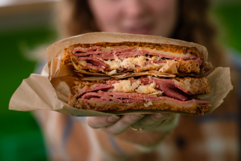Woman holding up a Reuben sandwich that is cut in half.