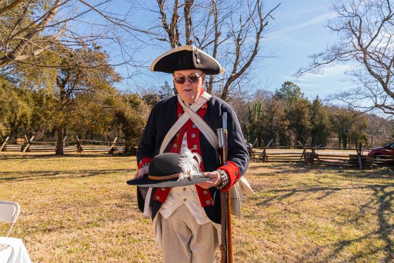 Revolutionary War soldier holding a black hat with a feather on it.