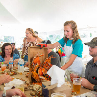 Girl serving crabs to a table of people drinking beer and talking.