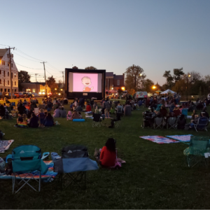 big movie screen with people watching the movie on blankets in Riverfront Park. Sunset in the background