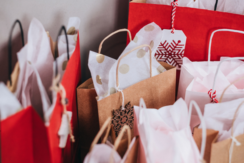 7 shopping backs with in colors of red and natural kraft with white tissue paper in each bag and a snowflake tag hanging on the side of each bag