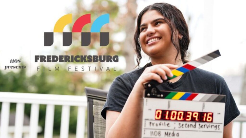 Fredericksburg Film Festival logo. Young woman with brunette hair, holding a timecode slate ("Clapper") that reads 'Profile; Second Servings' above '1108 Media,' sitting on a chair with a white railing and trees in the background.