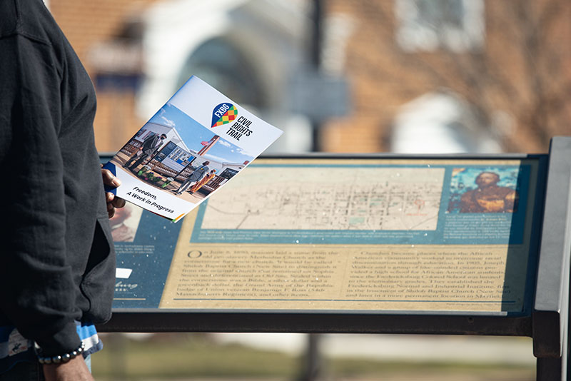 person holding Fredericksburg Civil Right Trail booklet while viewing wayside panel
