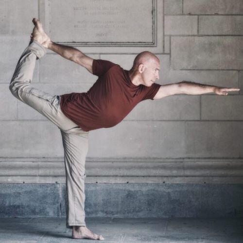 Man doing a yoga pose in a maroon shirt and brown pants