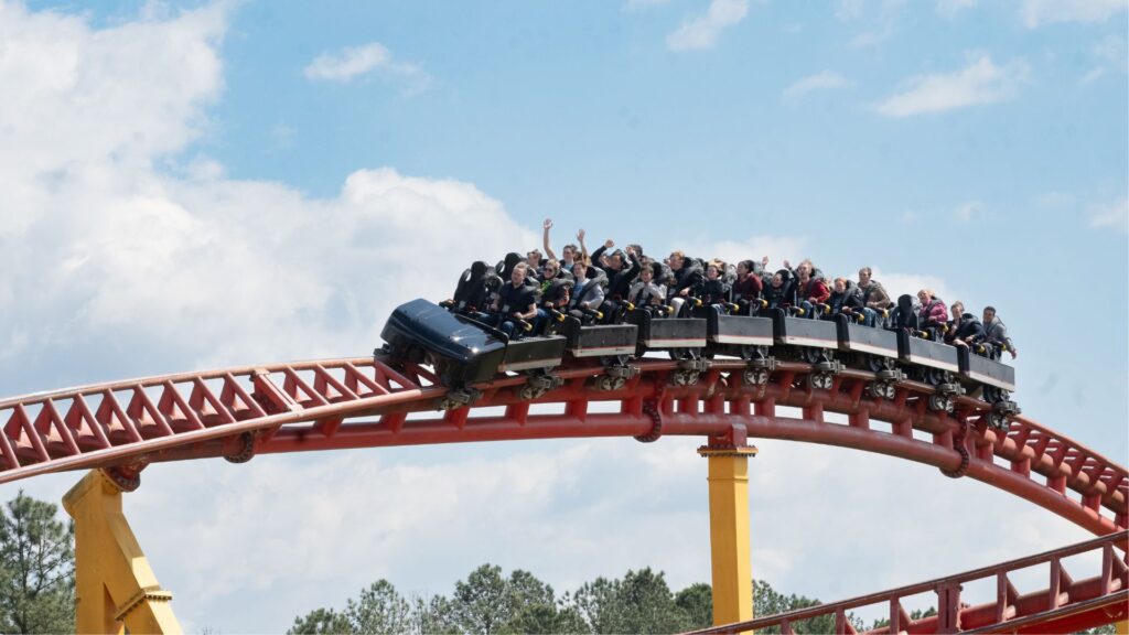Red, steel roller coaster track with black roller coaster car, filled with people riding