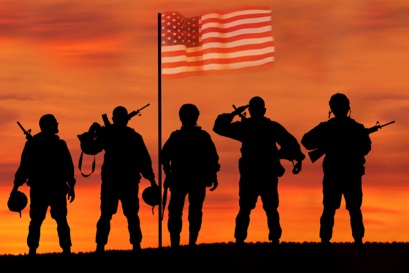 orange and read sunset. US flag flying. Black silhouettes if 5 soldiers as they look at the flag.