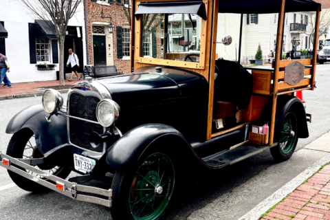model-a car parked on a street. Car is black and there is wood framing around seating cab