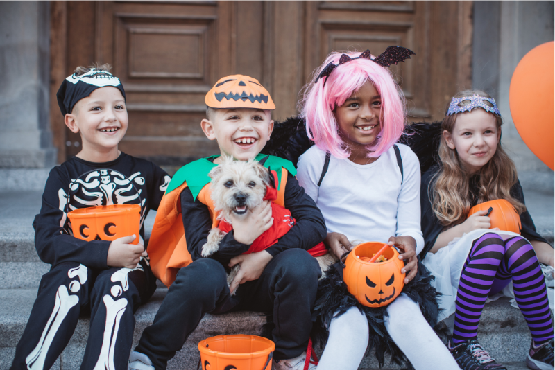 4 children in halloween costumes smiling and sitting on concrete steps