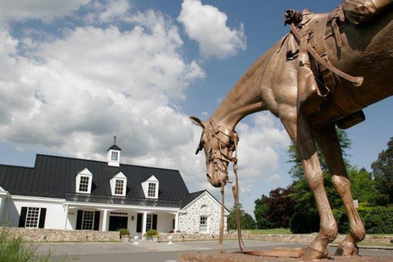 A bronze horse statue stands outside of a white building. 