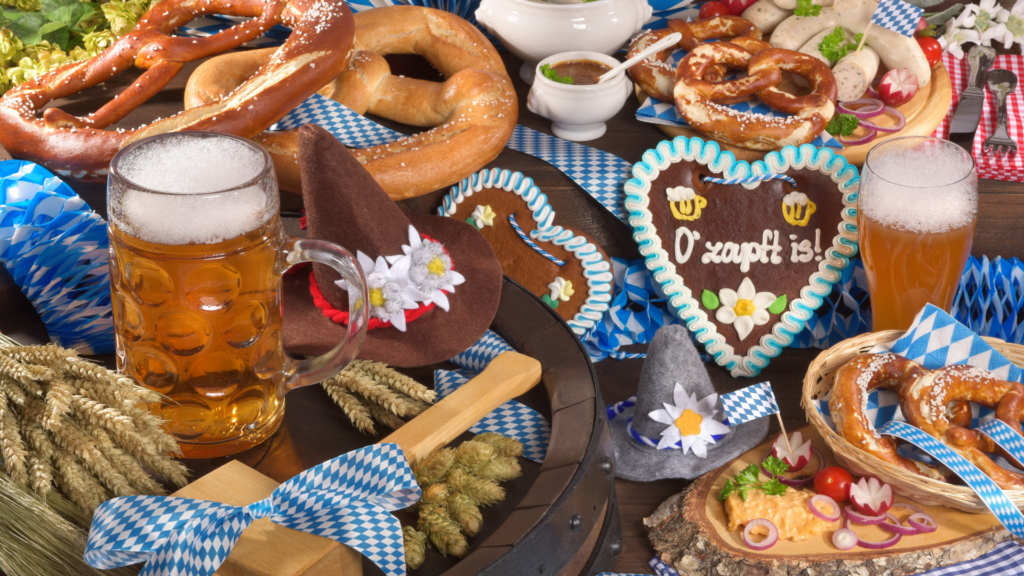 A variety of Oktoberfest Food items on a table. Big Pretzels, German Heart Cookies, Cheeses, Steins of beer