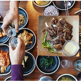 Two hands cheers-ing shot glasses over a table of food.