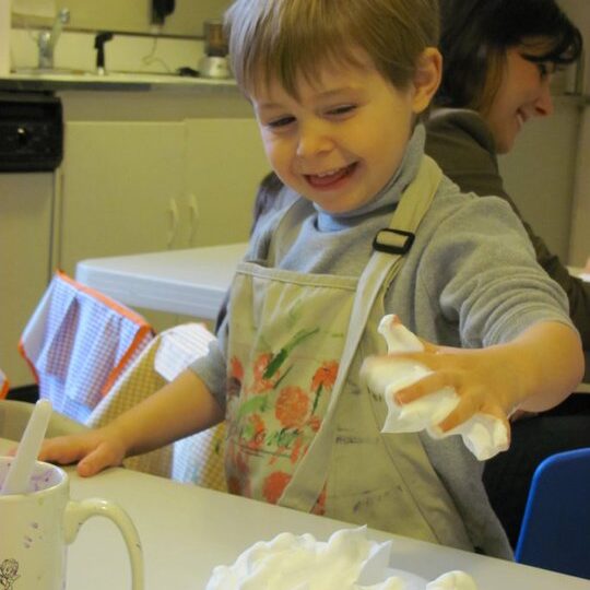 A young boy playing with foam and smiling.
