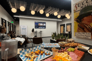 A group of professionals watches a presentation with food in the foreground.