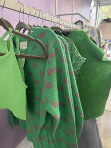 Green sweaters hanging on a rack in peacaloo boutique.