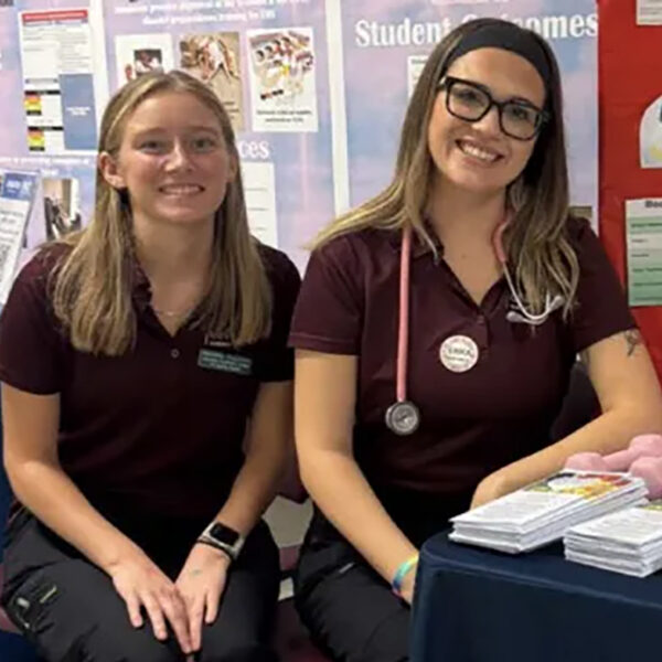 Two young nurses sitting at a table and smiling at the camera.
