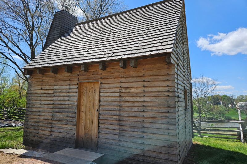 A rustic wooden cabin with a shingled roof and a single wooden door with a chimney.  