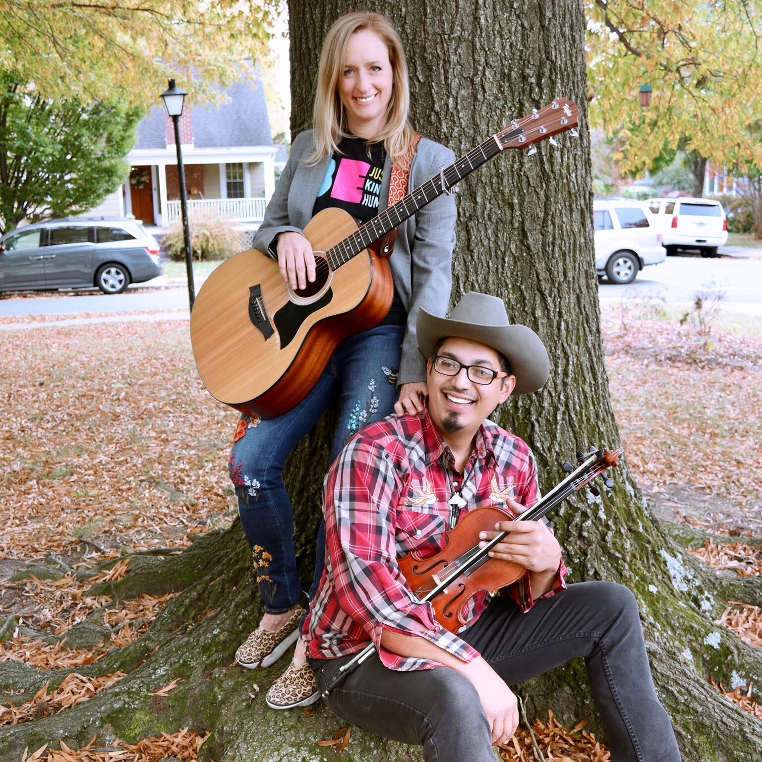 The peacemakers band, consisting of a man and woman both holding instruments leaning up against a tree.