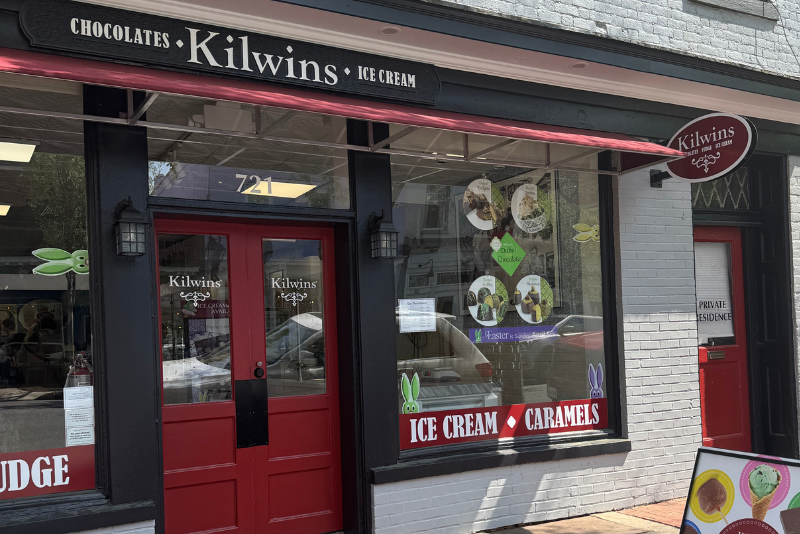 Exterior of Kilwins on Caroline Street in Downtown Fredericksburg. The storefront has red doors and large windows displaying products and advertisements.