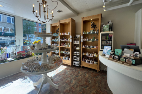 Inside of Pearlescent candle Co with merchandise on shelves and a tiered stand. The store features a chandelier, display cabinets with various candles, and a checkout counter with a computer monitor.