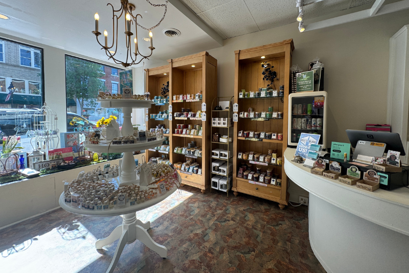 Inside of Pearlescent candle Co with merchandise on shelves and a tiered stand. The store features a chandelier, display cabinets with various candles, and a checkout counter with a computer monitor.