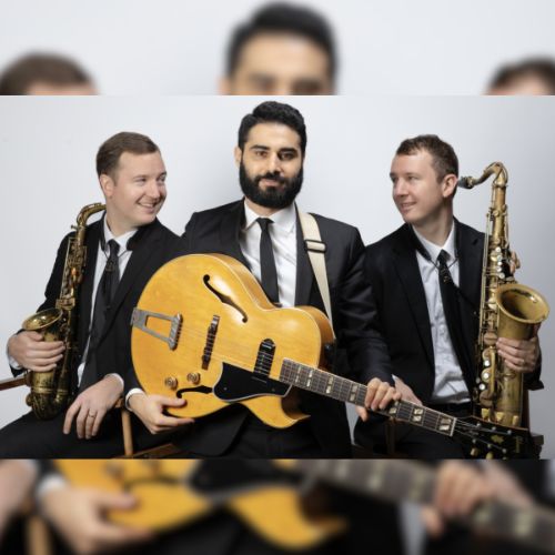 Three suited musicians pose together with a gold electric guitar and two saxophones against a light background, smiling and facing different directions.