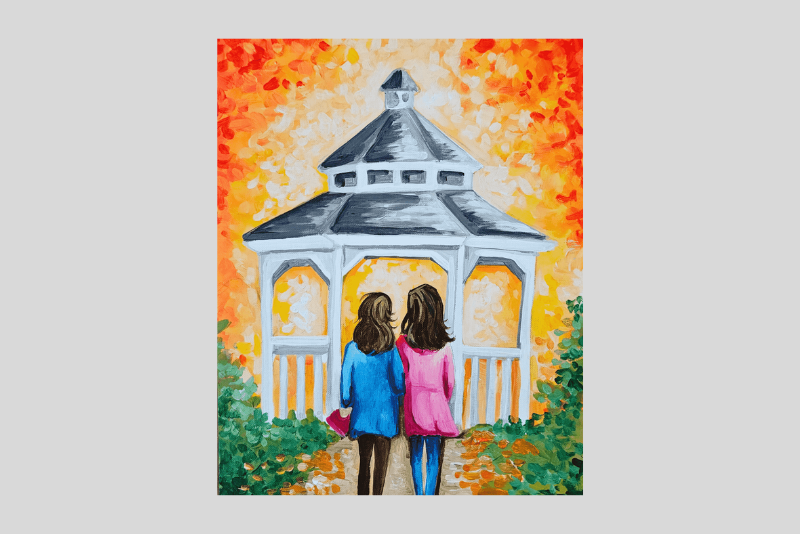 Two people in colorful autumn coats stand in front of a white gazebo with arched openings, framed by bright orange and yellow fall leaves and green foliage.