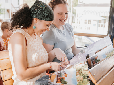 Two ladies sitting together on the trolley looking at a visitor guide and laughing.