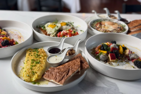Assorted plated dishes on a catering table, including a creamy polenta-like entrée, sliced meat, and several bowls of colorful salads with vegetables, herbs, and sauces.