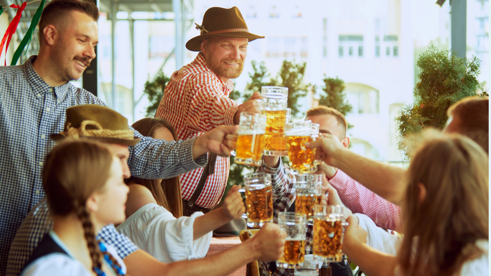 A group of people sitting and standing around a table, holding beer steins and toasting